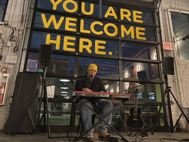 Keyboardist performing in front of a garage door that says "You Are Welcome Here"